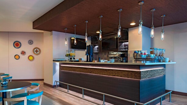 A modern bar area with a counter, seating, and decorative plates on the wall. - Fairfield by Marriott San Salvador (Antiguo Cuscatlán)