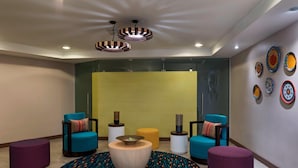 A modern lounge area with two blue armchairs, a round wooden coffee table, a patterned rug, and a yellow accent wall. - Fairfield by Marriott San Salvador (Antiguo Cuscatlán)