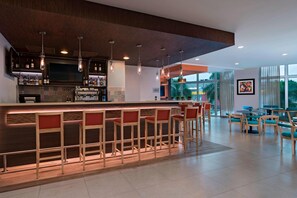 Zona de bar moderna con una barra alargada, varios taburetes e iluminación colgante.