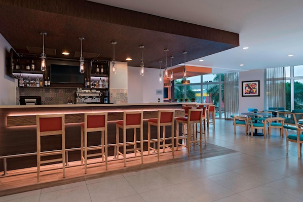 A modern bar area with a long counter, multiple stools, and overhead lighting.