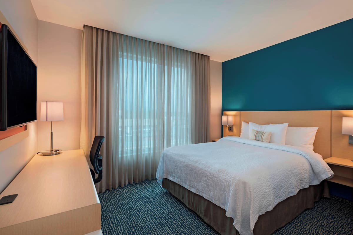 A hotel room with a bed, a desk, a chair, a TV, and a window with curtains.