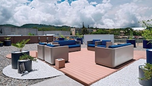 An outdoor seating area with sofas and planters, surrounded by a wooden deck and gravel. - Fairfield by Marriott San Salvador (Antiguo Cuscatlán)