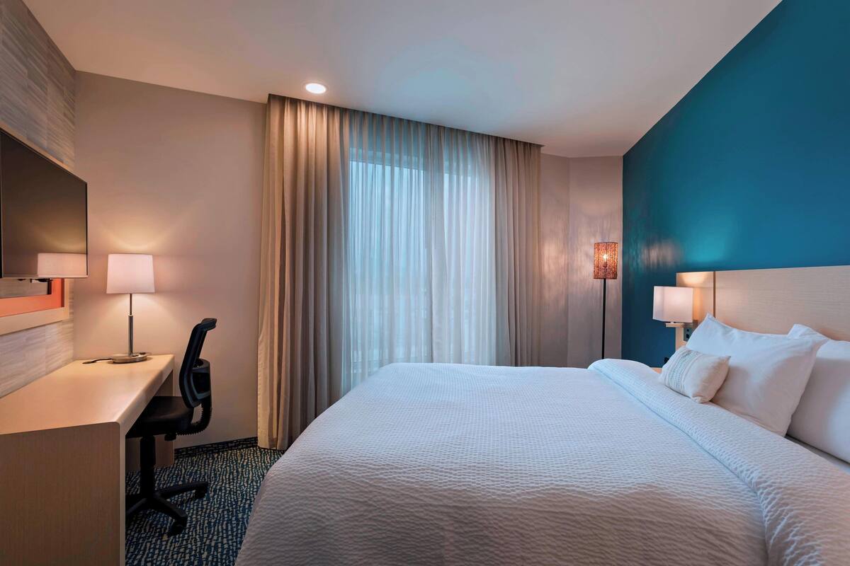 A hotel room with a bed, desk, chair, and two lamps.