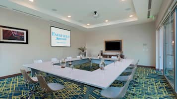 A conference room with a large table, chairs, a projector screen, and a television.