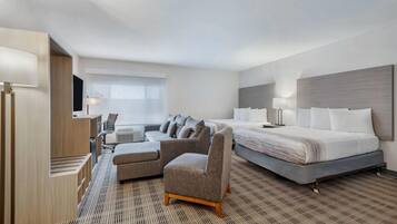 A hotel room with a bed, two armchairs, a sofa, a desk with a lamp, and a television.