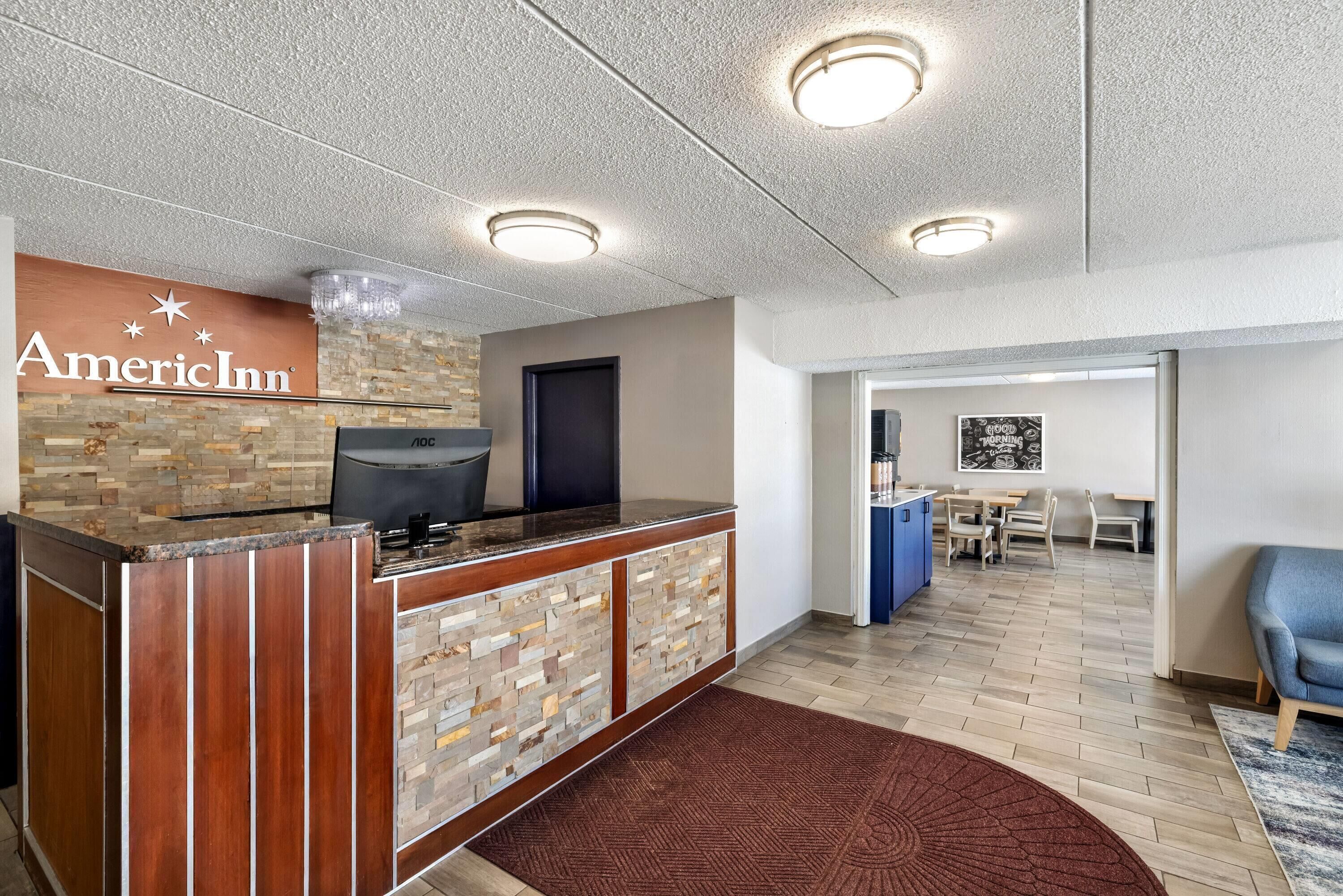 Zona de recepción de hotel con pared de piedra, mostrador de recepción y vista hacia un comedor.