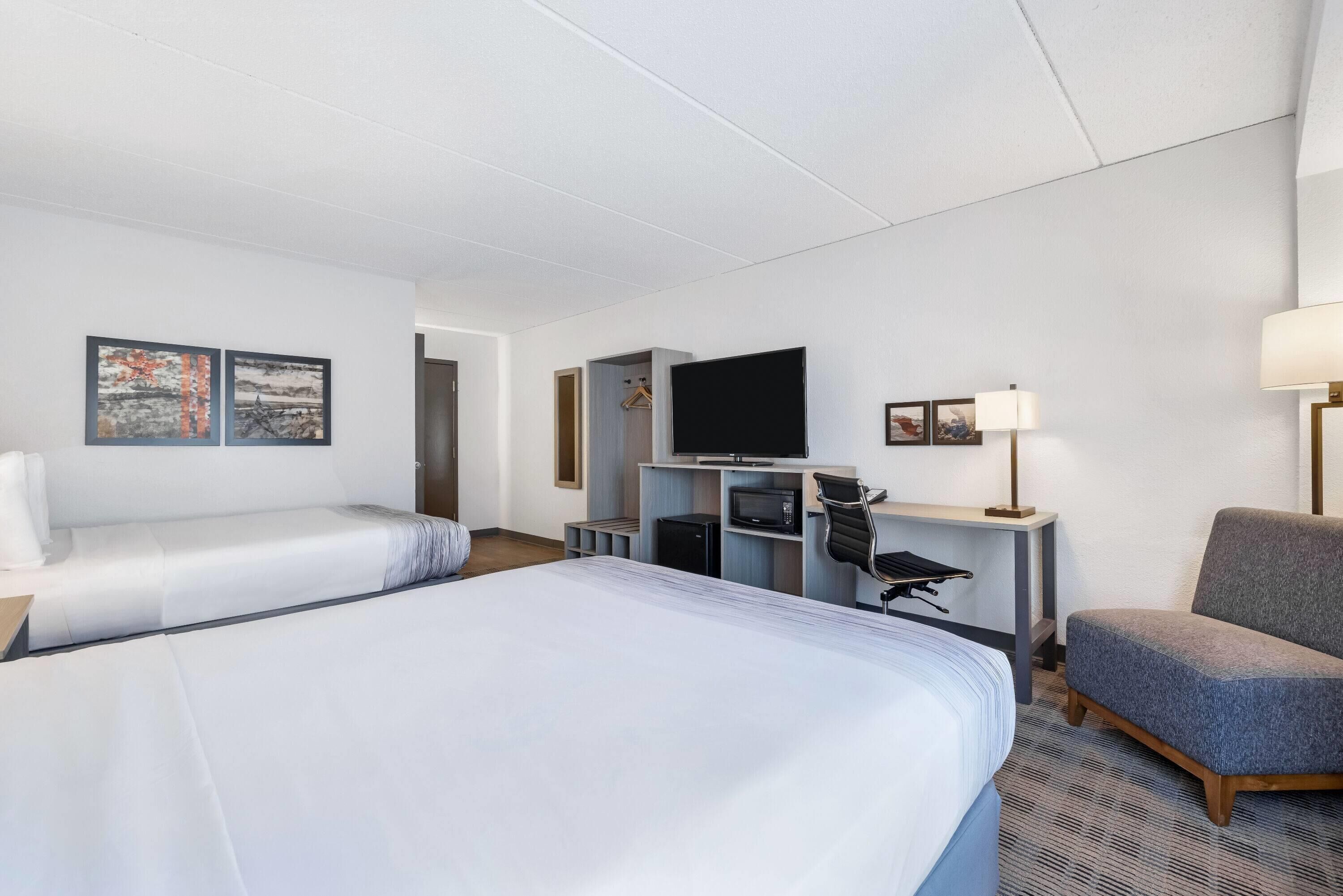 A hotel room with two beds, a television, a desk with a lamp, and artwork on the walls.