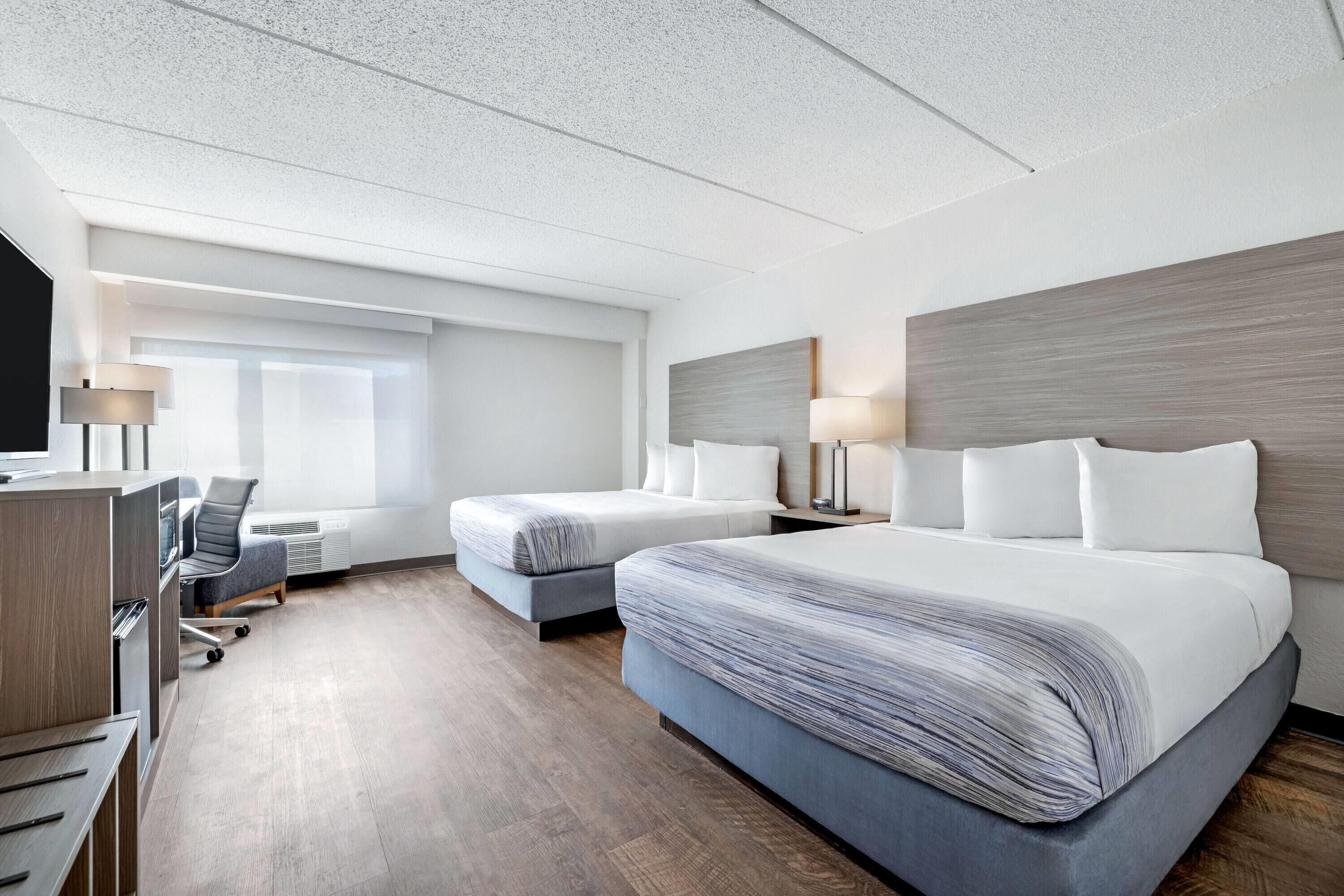 A hotel room with two beds, a desk, a chair, and a television.