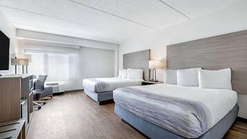 A hotel room with two beds, a desk, a chair, and a television.