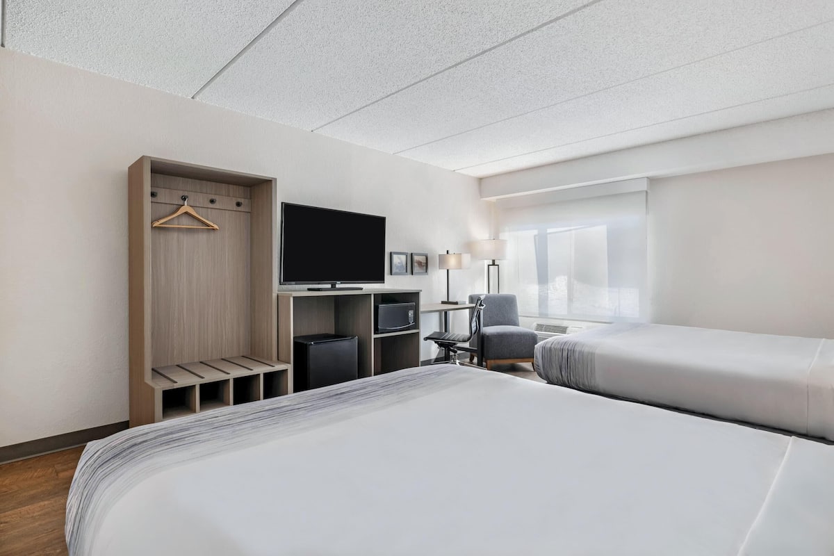 A hotel room with a bed, a TV, a desk, a chair, and a wardrobe.