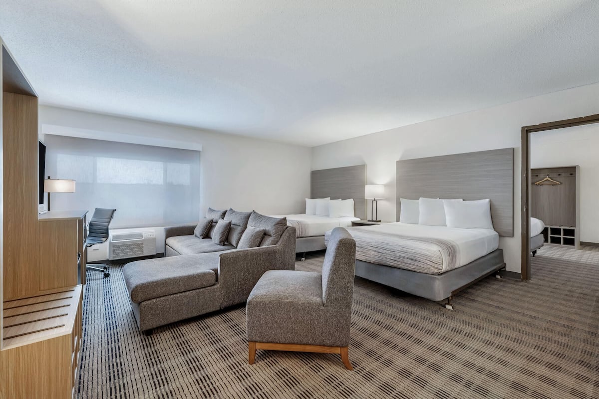 A hotel room with a bed, two armchairs, a sofa, a desk with a chair, and a TV.