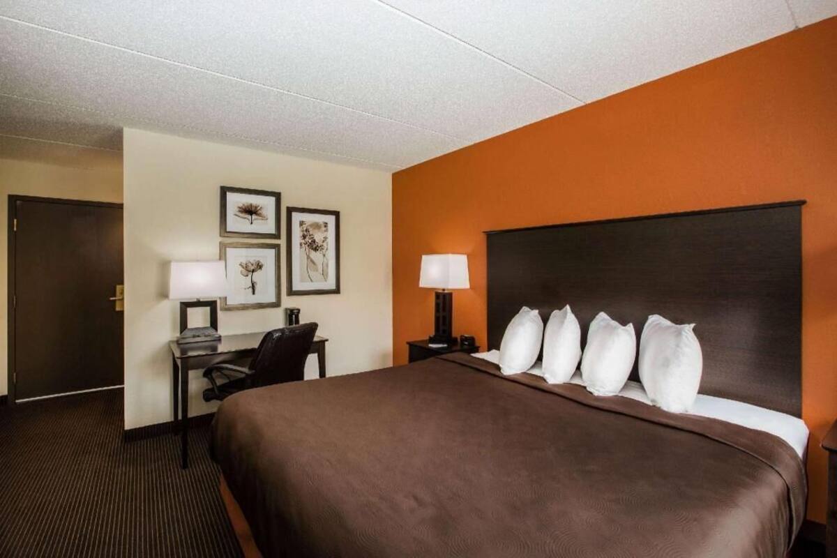 A hotel room with a large bed, a desk with a chair, a lamp, and framed artwork on the wall.