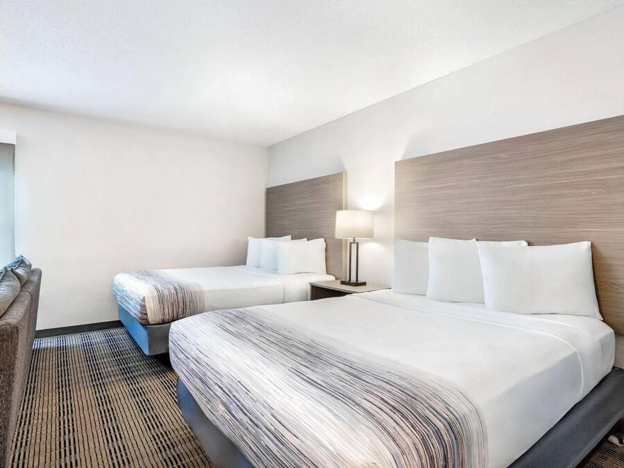 A hotel room with two beds, a nightstand with a lamp, a chair, and a large window.