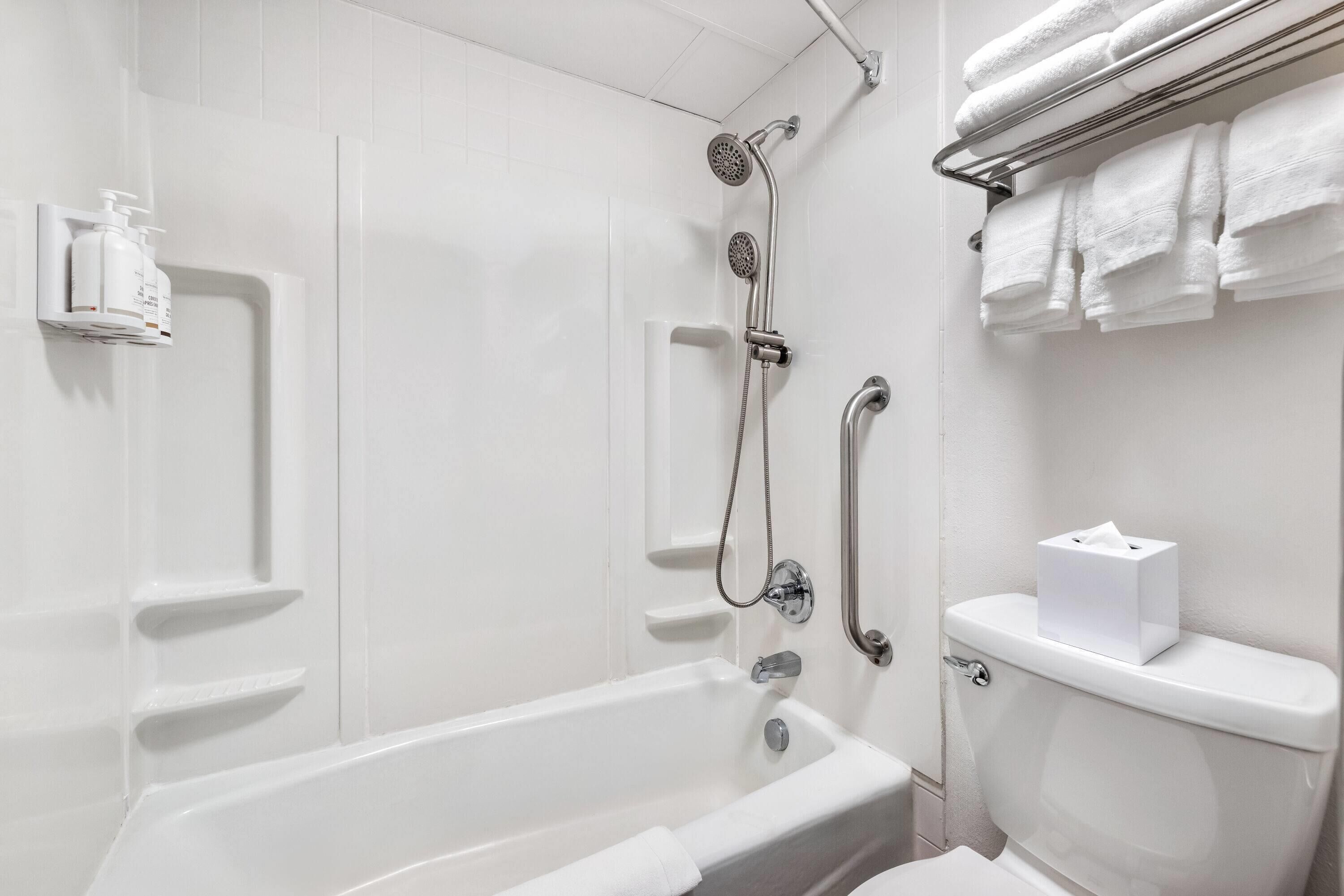 A white bathroom with a bathtub, a shower, and a toilet. There are white towels and a tissue box on the toilet.
