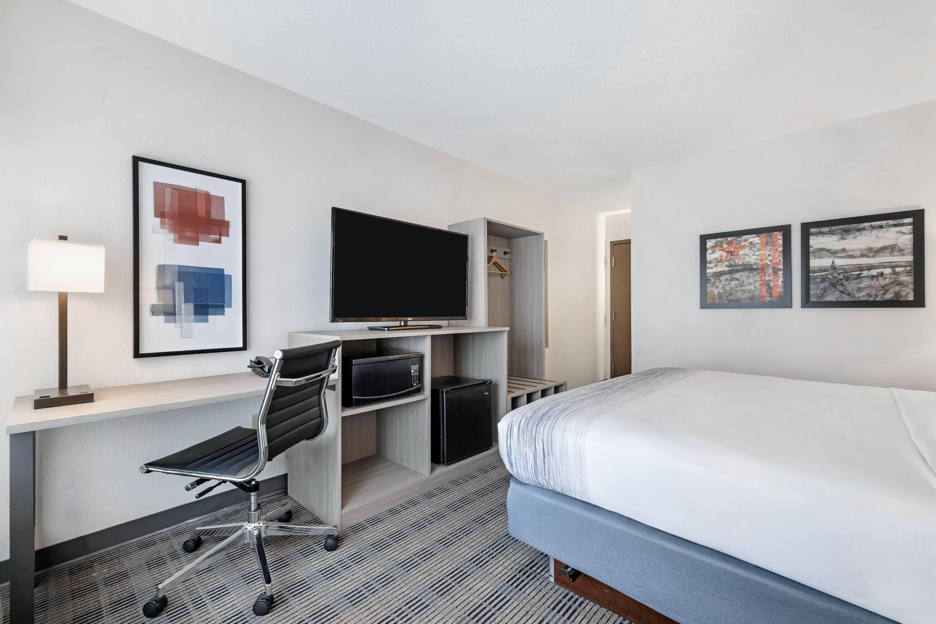 A hotel room with a bed, a desk with a chair, a television, and artwork on the walls.