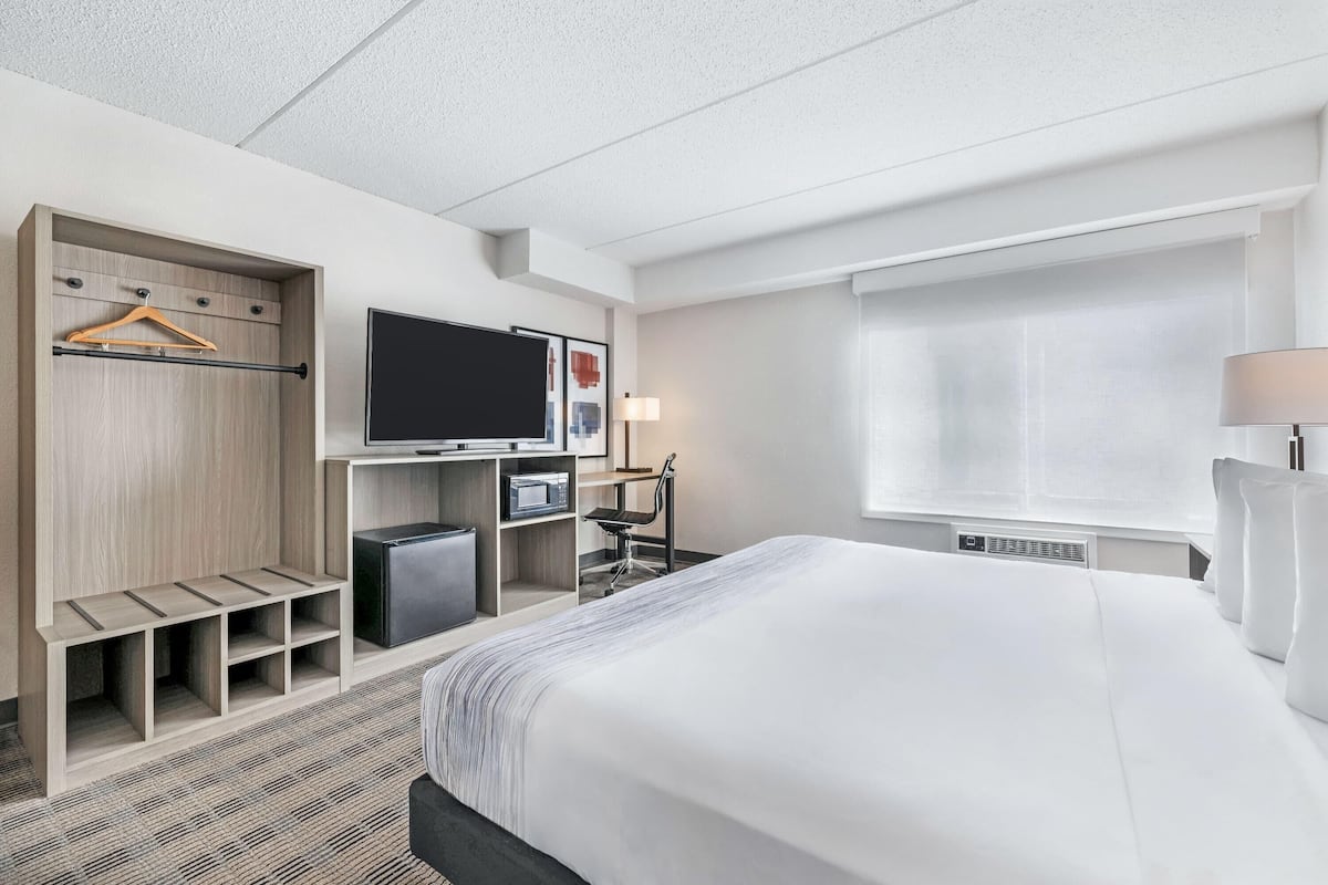 A hotel room with a bed, a TV, a desk with a chair, a wardrobe, and a window.