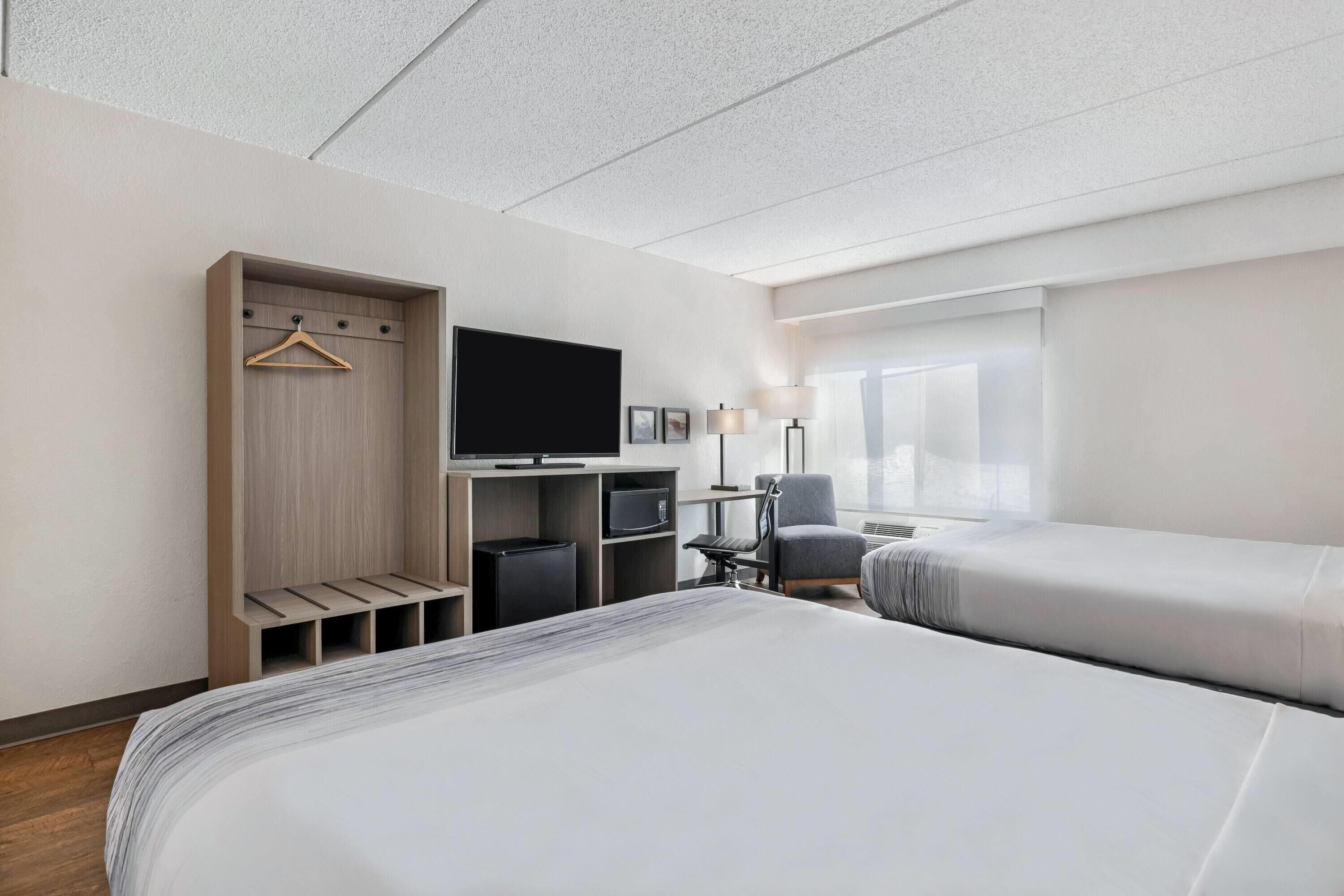Ett hotellrum med en säng, en tv, ett skrivbord med en stol, en garderob och ett fönster.