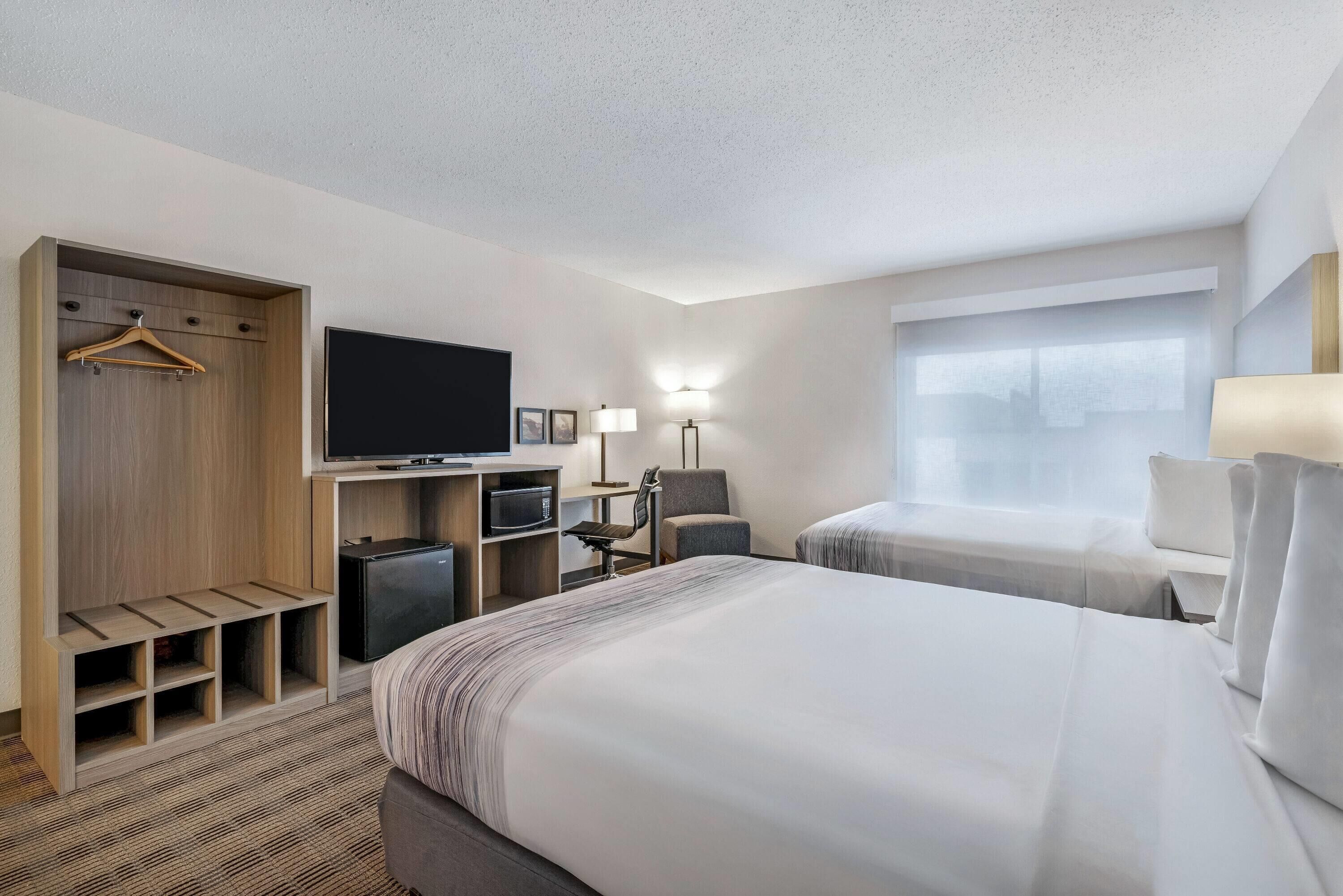A hotel room with a bed, a TV, a desk with a computer, a chair, a wardrobe, and a window.