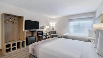 A hotel room with a bed, a TV, a desk with a computer, a chair, a wardrobe, and a window.