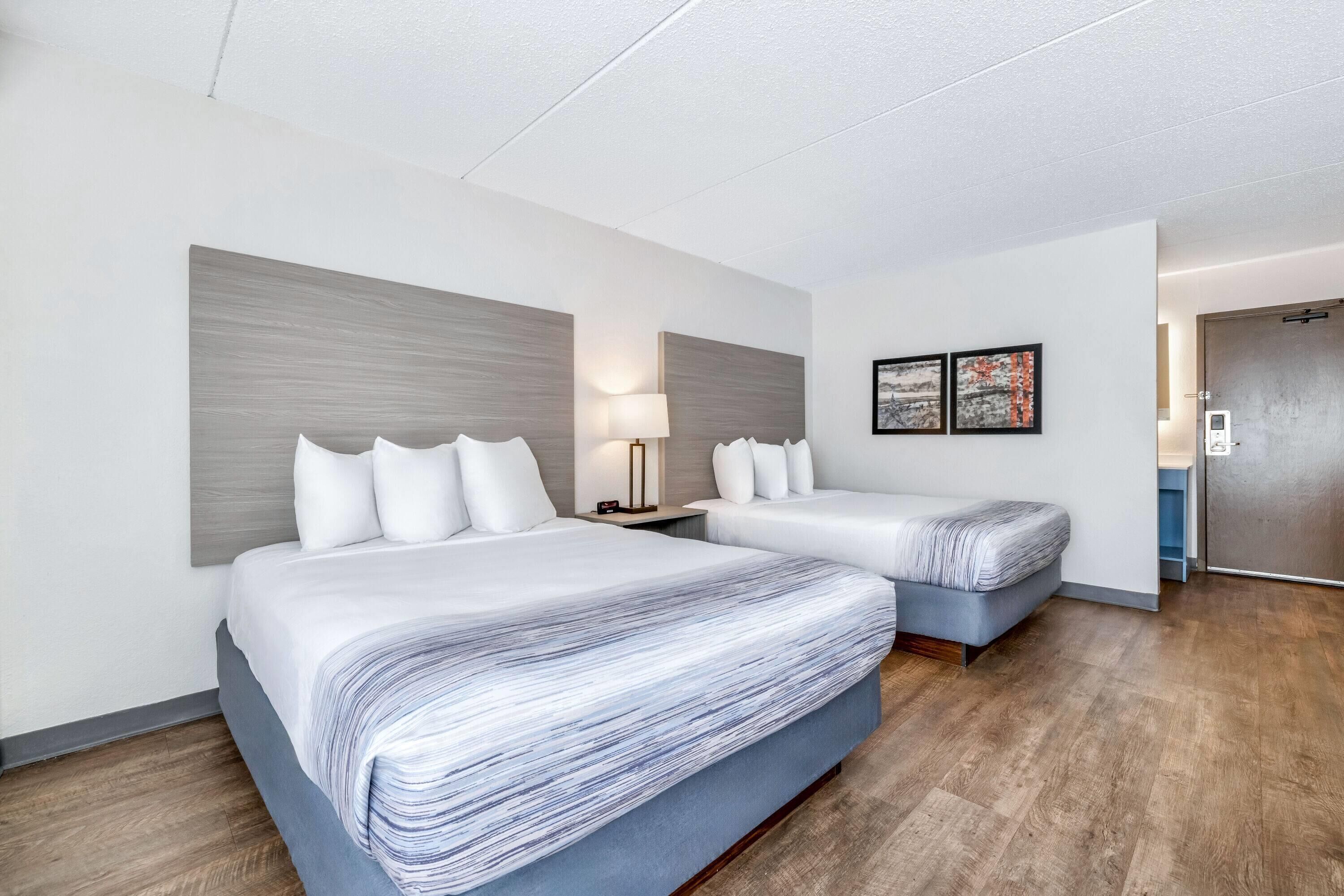 A hotel room with two beds, a nightstand, a lamp, and two framed pictures on the wall.