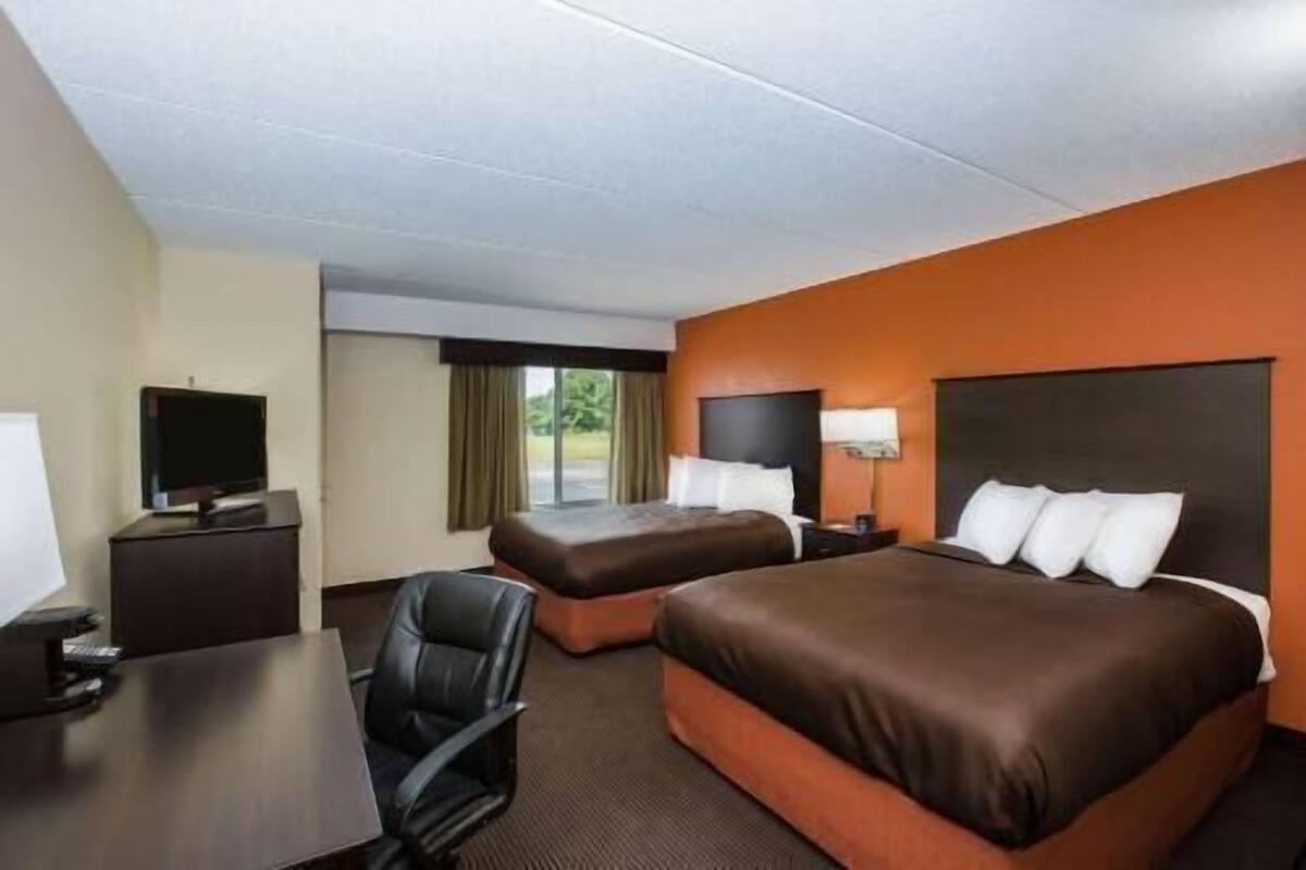 A hotel room with two beds, a desk, a chair, a TV, and a window with curtains.