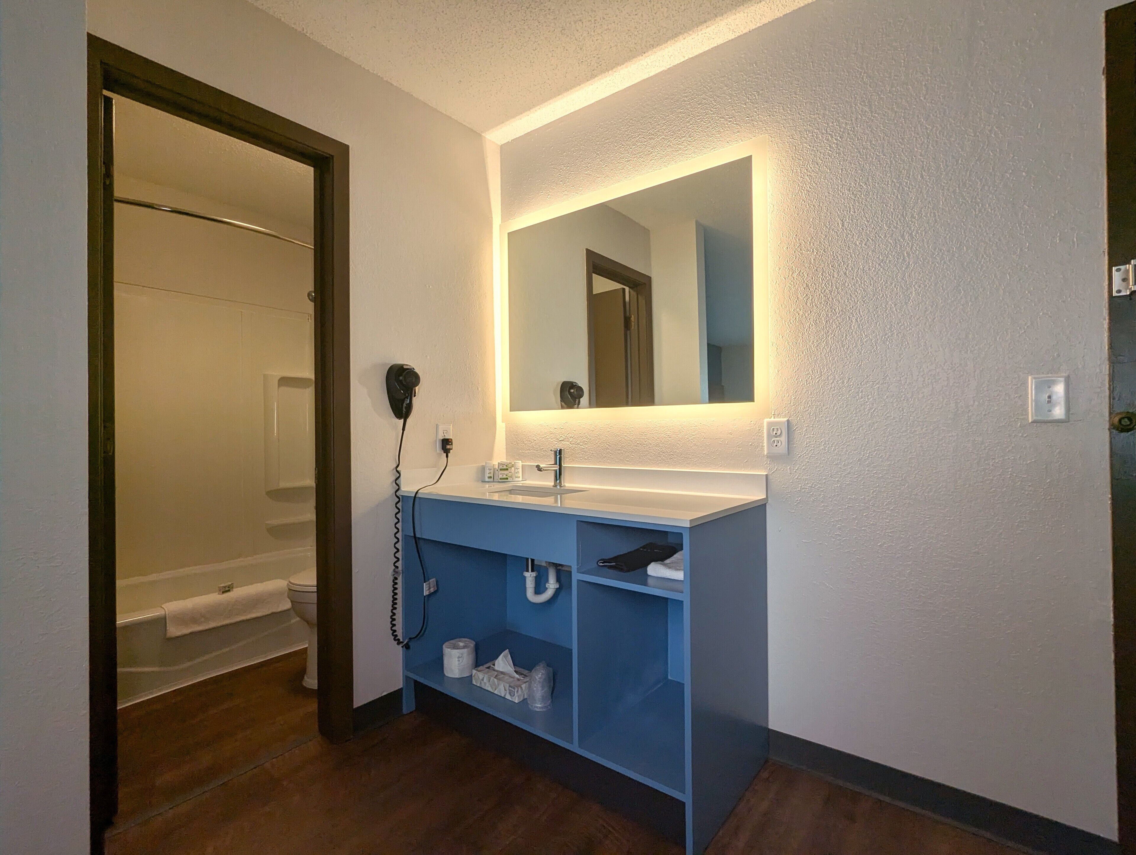 A bathroom with a white sink, blue vanity, and a mirror above it. There is a towel rack on the wall and a toilet visible in the background.
