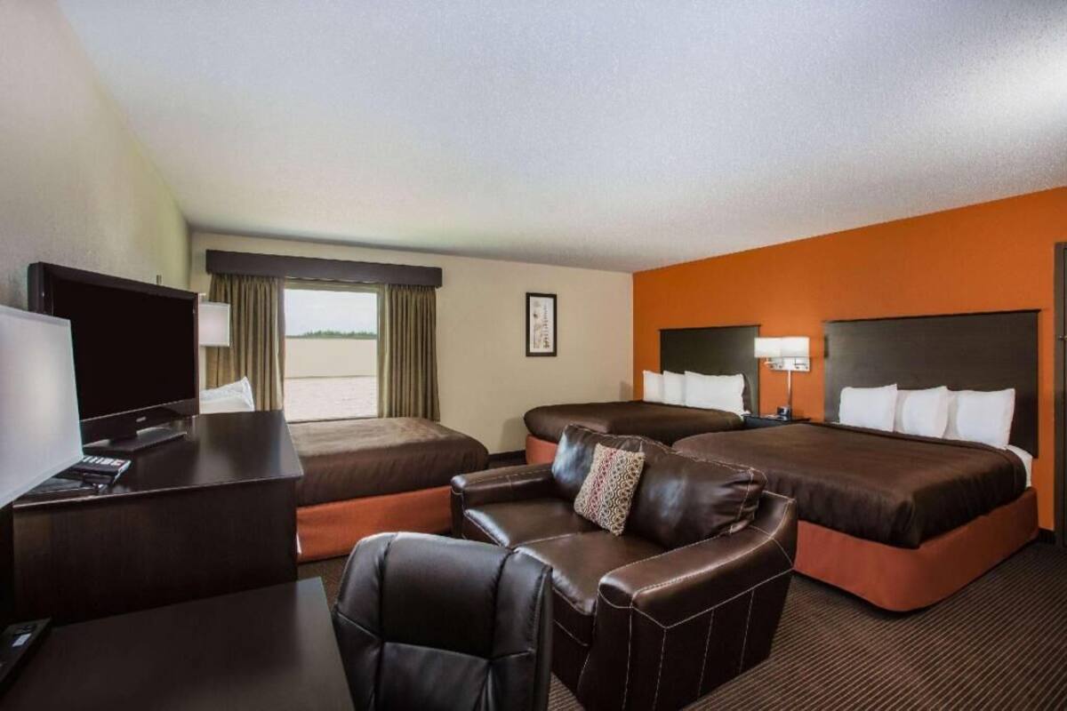 A hotel room with two beds, a desk, a TV, and a leather chair.