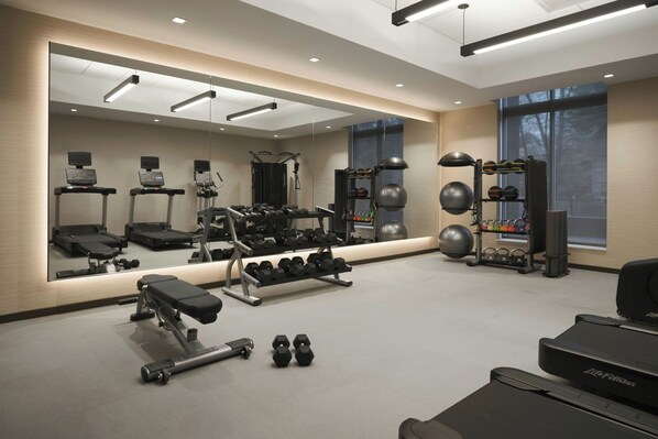 Un gimnasio moderno con equipo de ejercicio, un espejo grande y amplias ventanas.