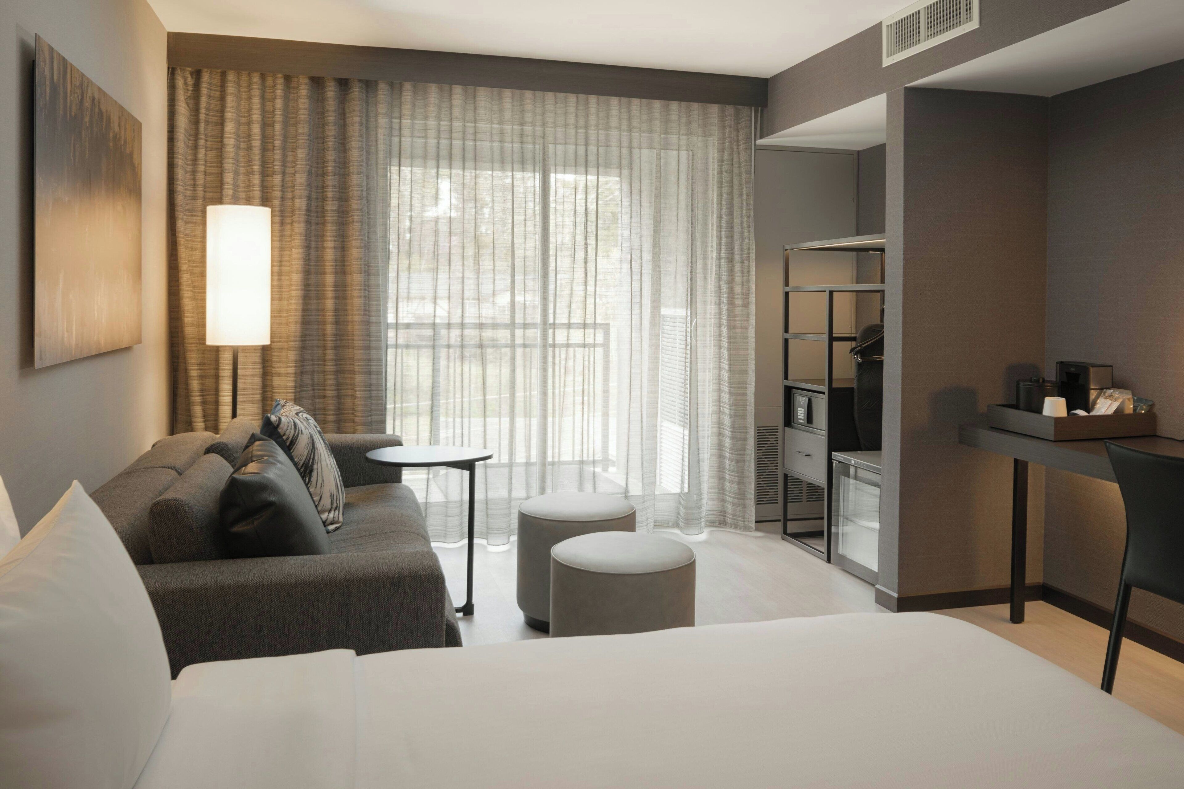A modern hotel room with a large bed, a sofa, a small table, and a desk.