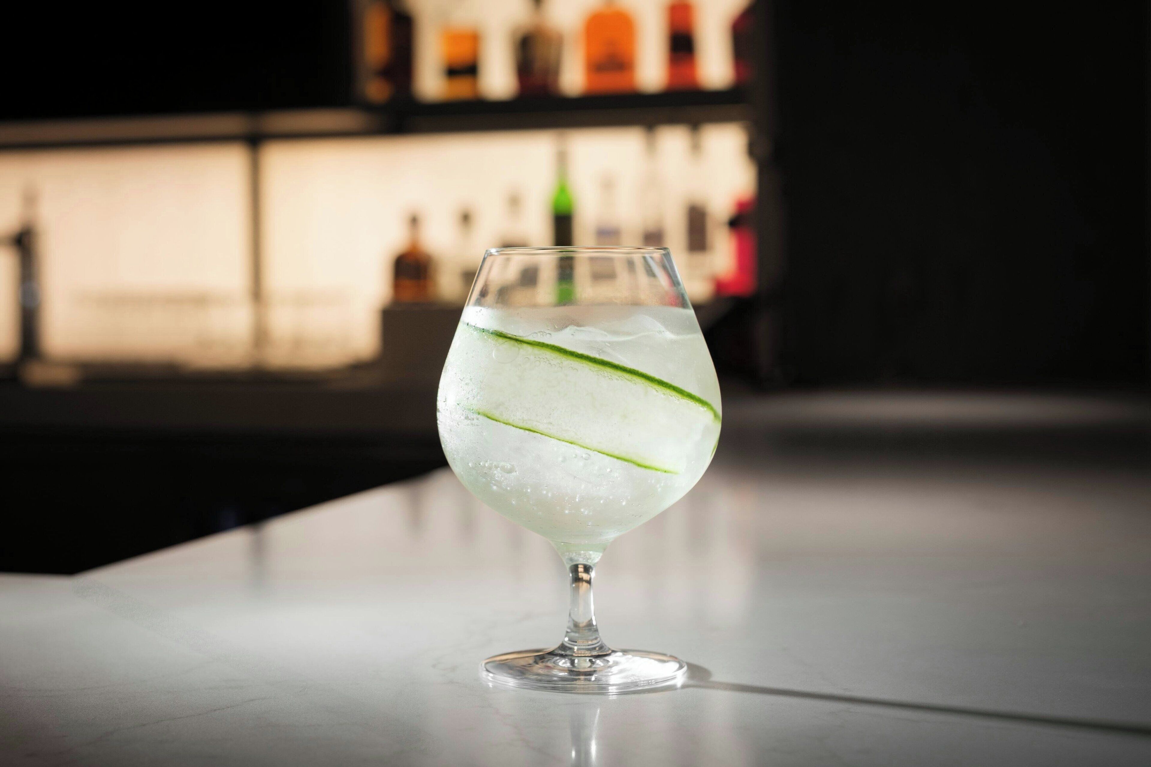 Ein Cocktailglas mit Eiswürfeln und einem Limettenschnitzchen auf einer Bartheke.