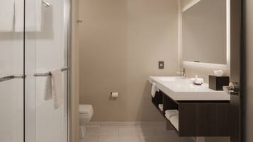 Un baño moderno con cabina de ducha de vidrio, un lavabo blanco con mueble oscuro y un espejo grande sobre el lavabo.