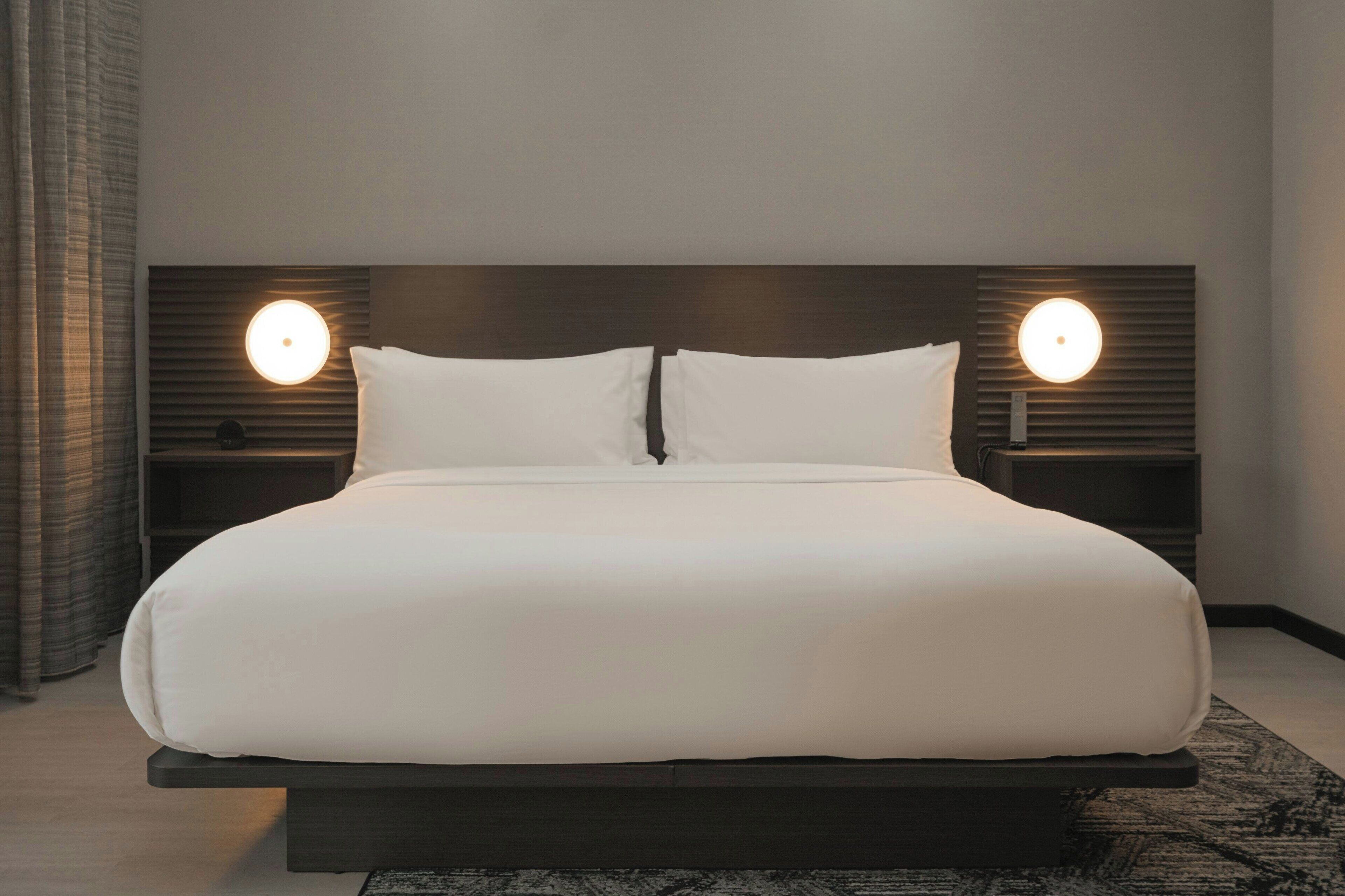 Una cama grande con cabecera oscura y dos lámparas de noche.