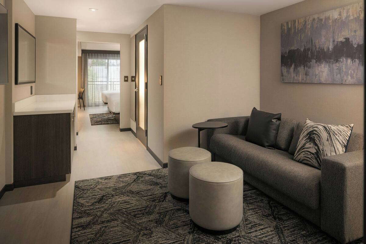 A modern hotel room with a sofa, ottomans, a small table, and a painting on the wall.