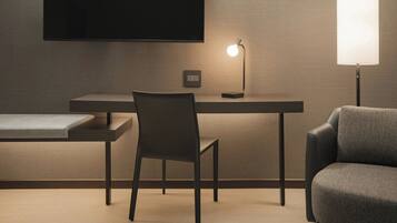A modern room with a desk, a chair, a sofa, a TV mounted on the wall, and a lamp on the desk.