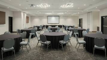 A conference room with multiple tables and chairs, a projector screen, and a carpeted floor.