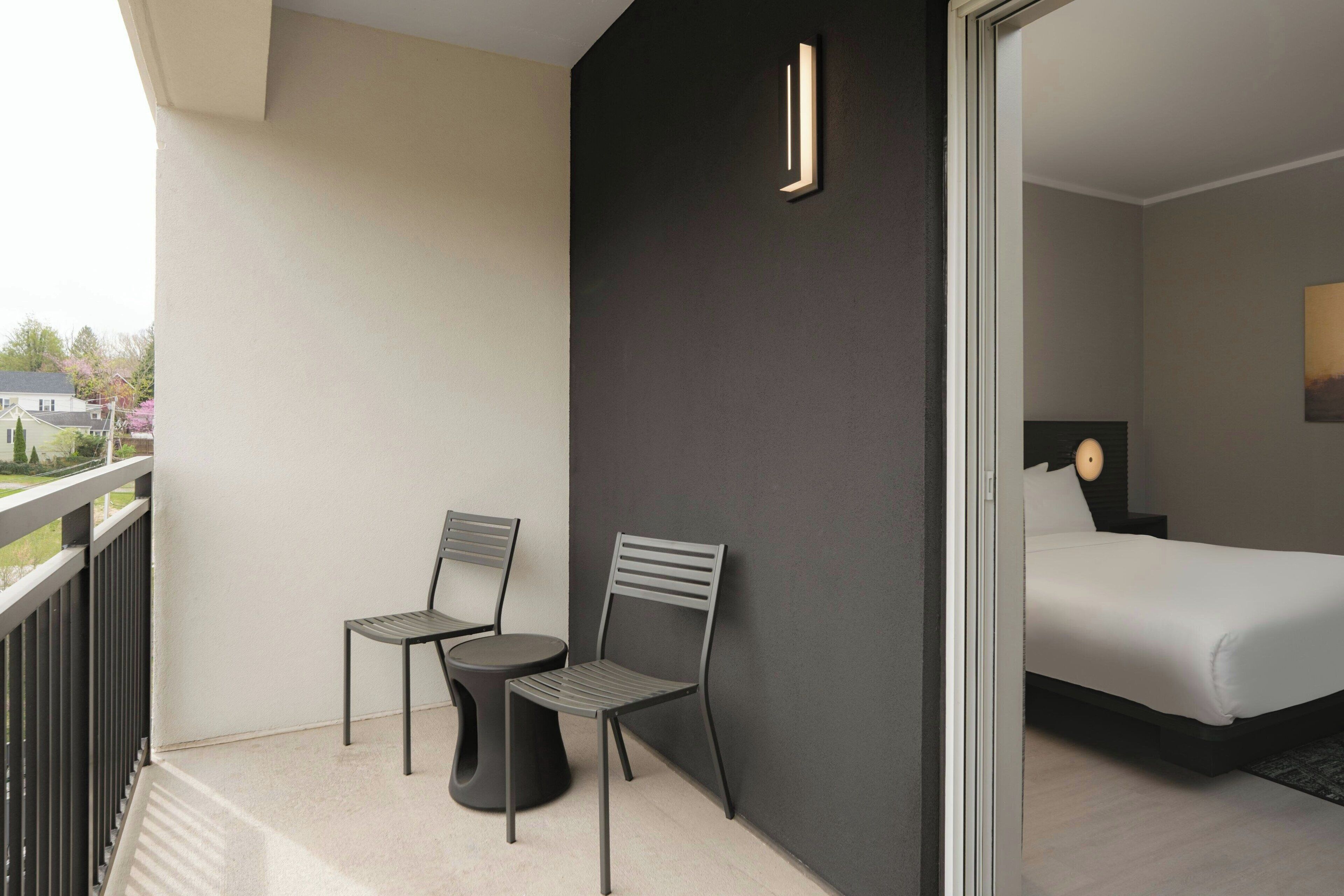 A modern hotel room with a balcony, a bed, and two chairs.