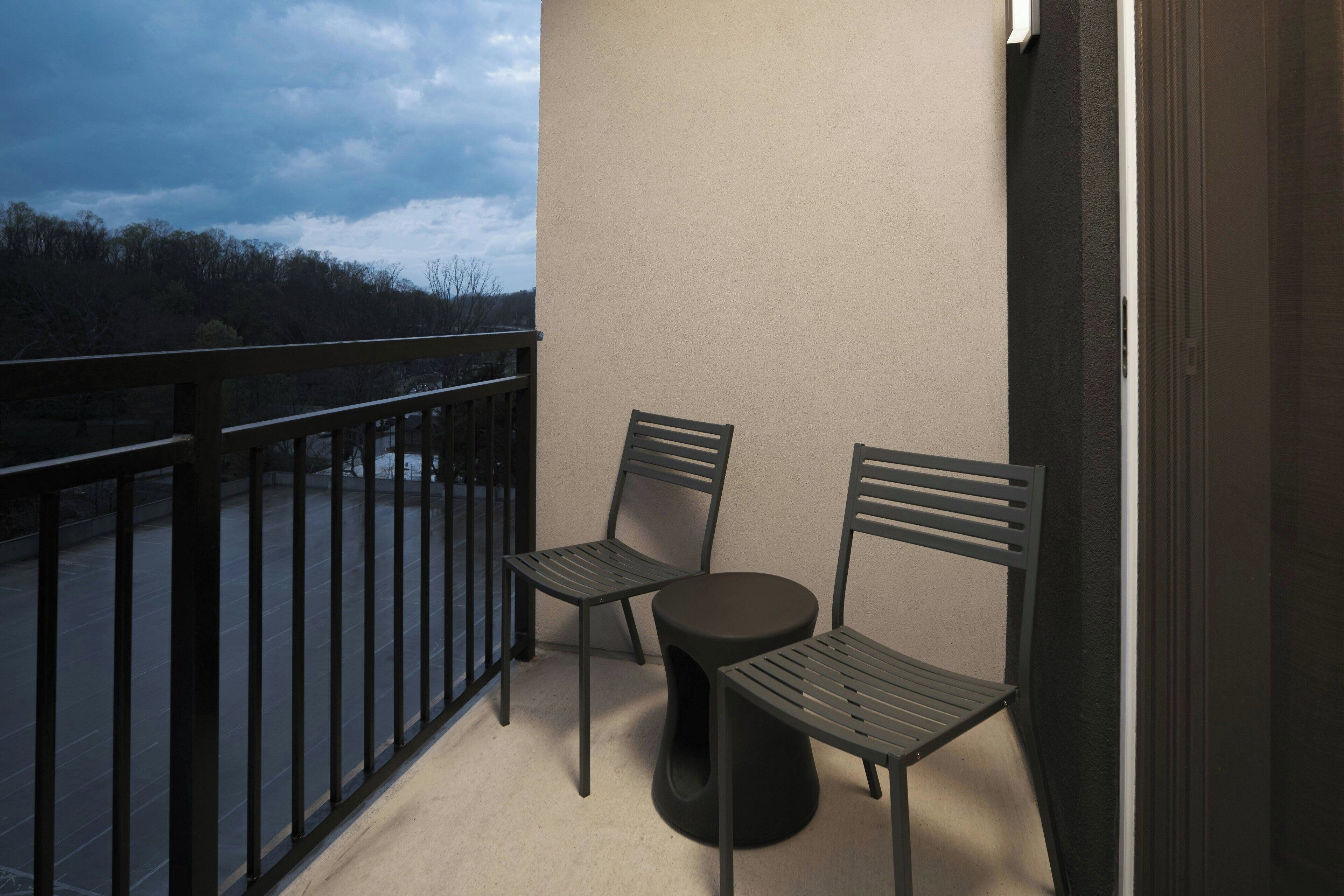 A balcony with two chairs and a small round table, overlooking a forested area.