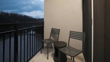 A balcony with two chairs and a small round table, overlooking a forested area.