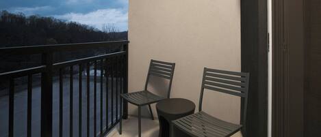 A balcony with two chairs and a small round table, overlooking a forested area.