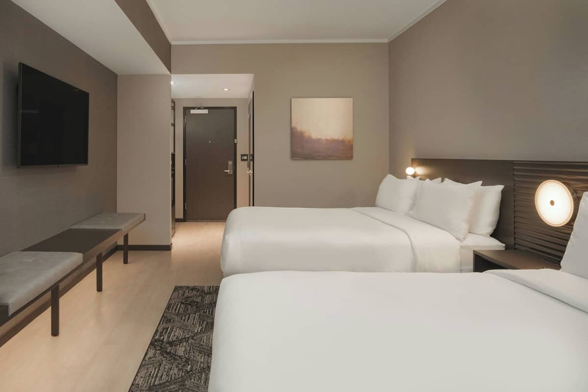 A hotel room with two beds, a bench, a flat-screen TV, and a painting on the wall.