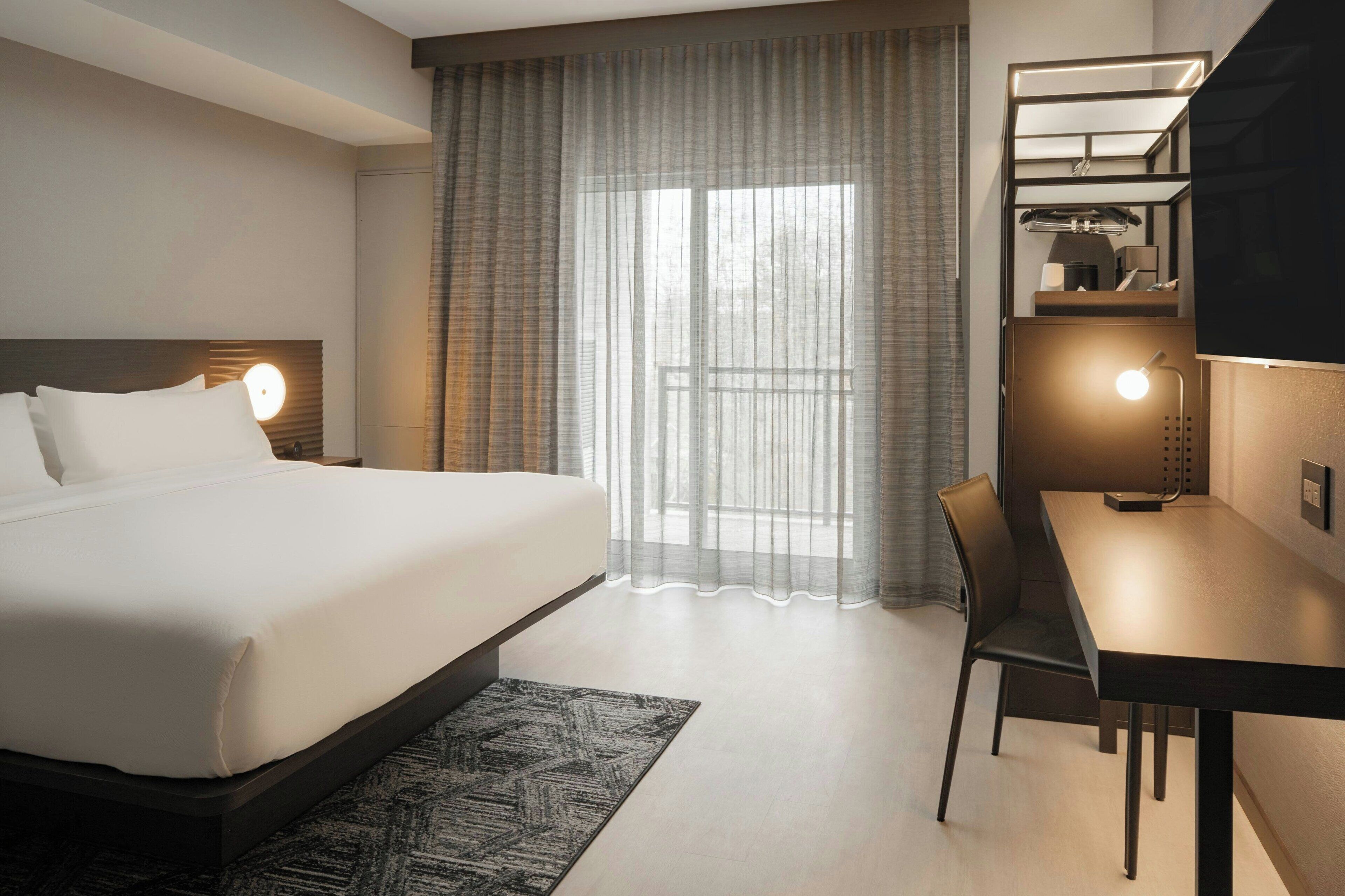 Een hotelkamer met een bed, een bureau, een stoel, een televisie en een raam met gordijnen.