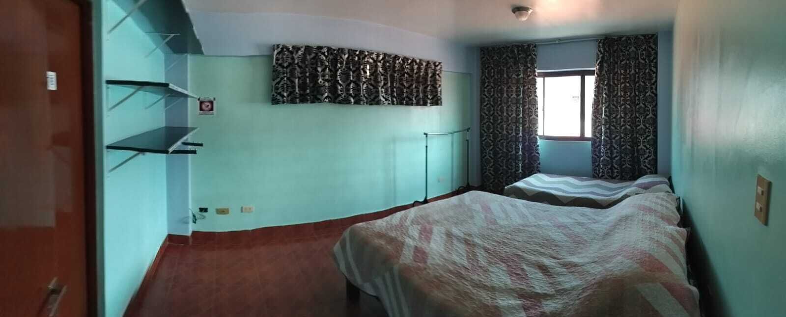 A room with two beds, a radiator, a patterned curtain, and a shelf unit.