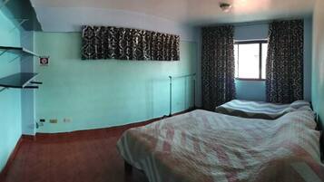 A room with two beds, a radiator, a patterned curtain, and a shelf unit.