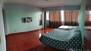 A room with a bed, a television on the wall, patterned curtains, and a tiled floor. - Space (Cochabamba)