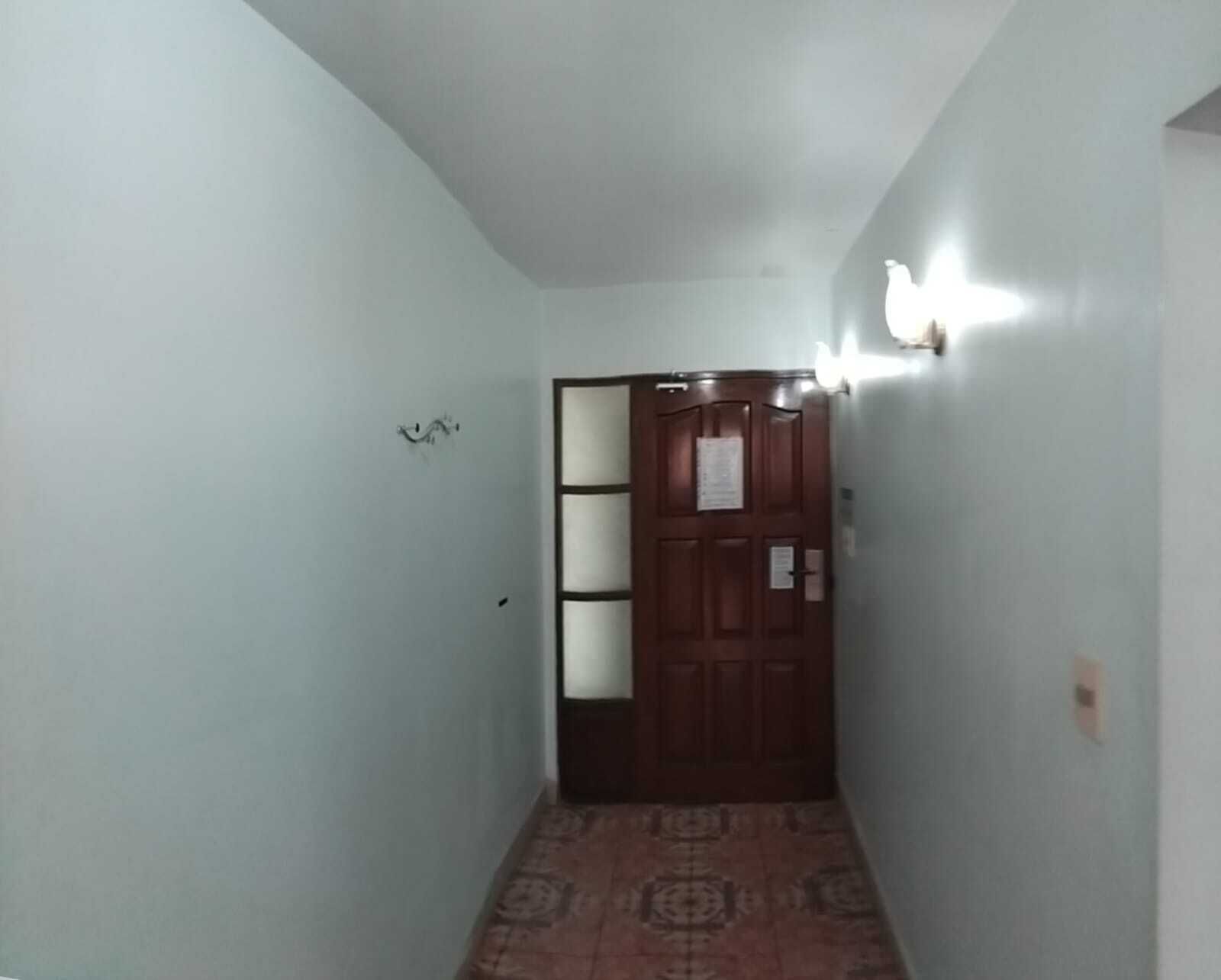 A narrow hallway with a patterned floor, a wooden door with a glass panel, and wall-mounted lights.