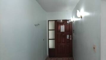 A narrow hallway with a patterned floor, a wooden door with a glass panel, and wall-mounted lights.