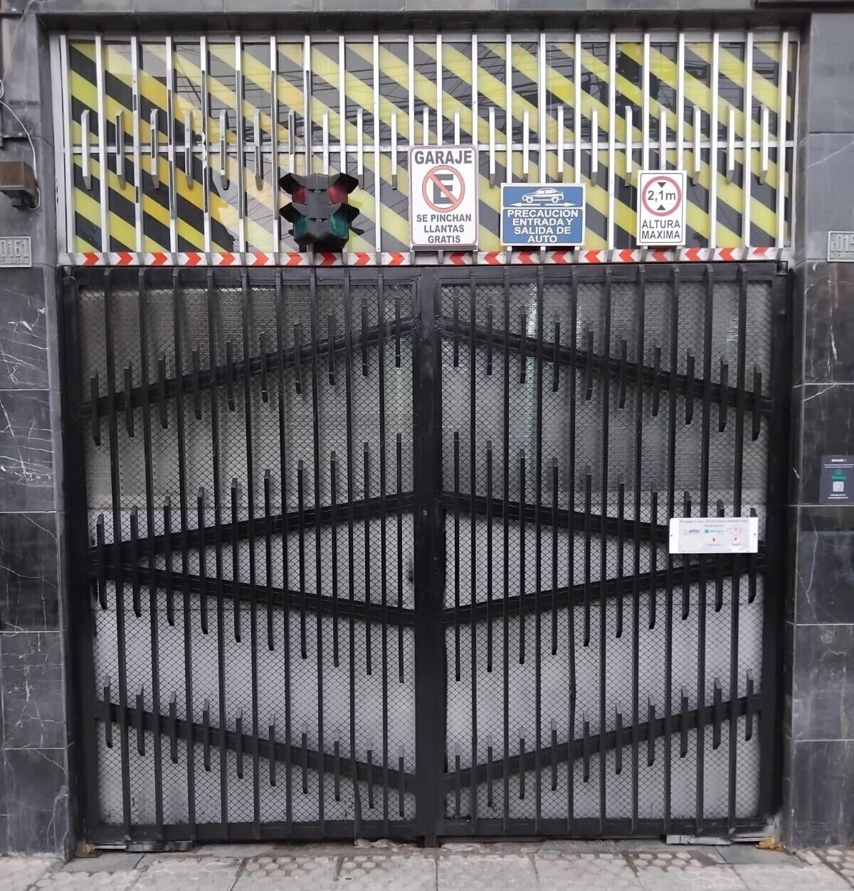 Une entrée fermée par un portail et protégée par une clôture métallique, un panneau indiquant la présence d’un garage et des panneaux signalant une hauteur maximale autorisée.