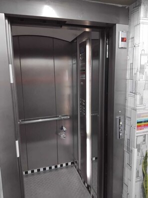 A metallic elevator interior with a control panel and a cityscape mural on the wall. - Space (Cochabamba)