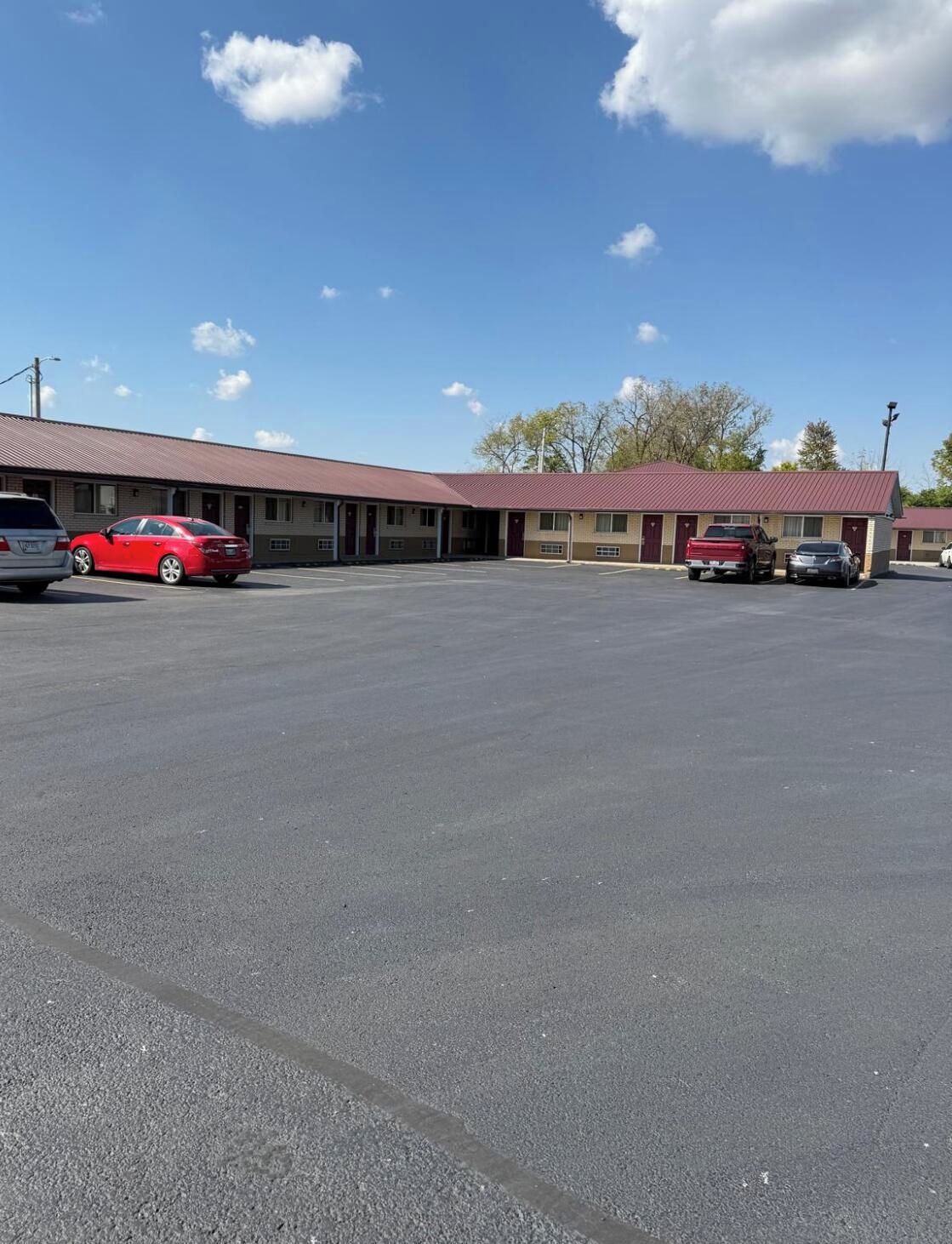 Un motel avec un parking, plusieurs voitures garées et un ciel dégagé.