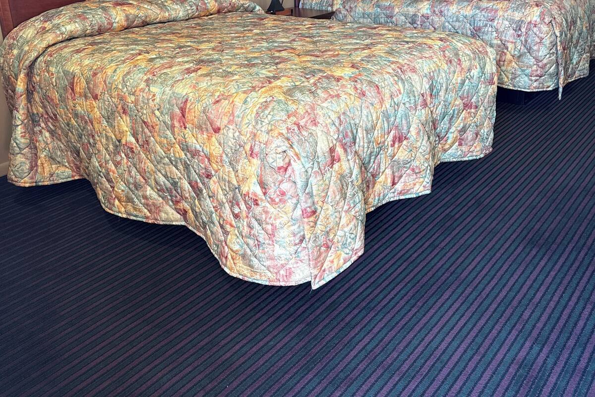 Habitación de hotel con dos camas, una mesita de noche con lámpara y piso alfombrado.